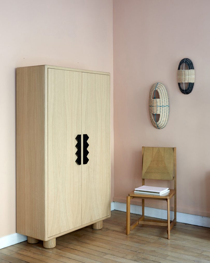 tall light wood armoire with chair and 3D wall art in a styled space