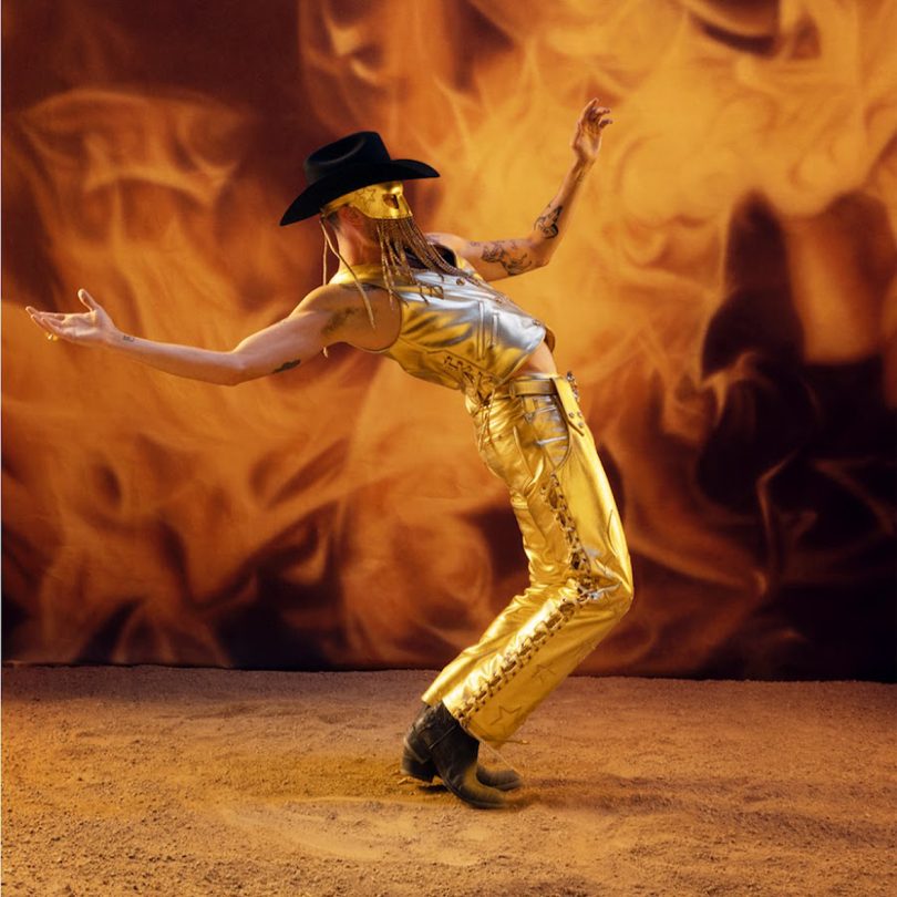 mysteriously clad cowboy dressed in gold pants and a mask posing in front of smoke