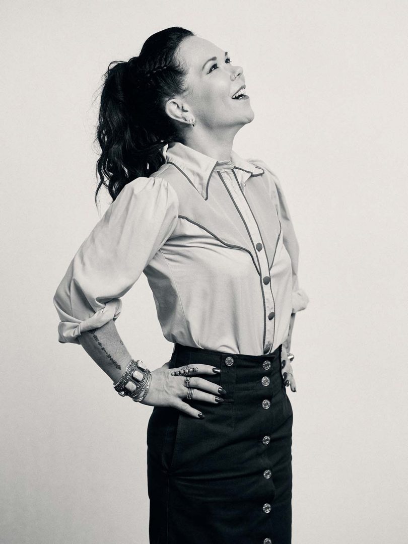 black and white photo of light-skinned woman with dark hair pulled back wearing western wear with her hands on her hips