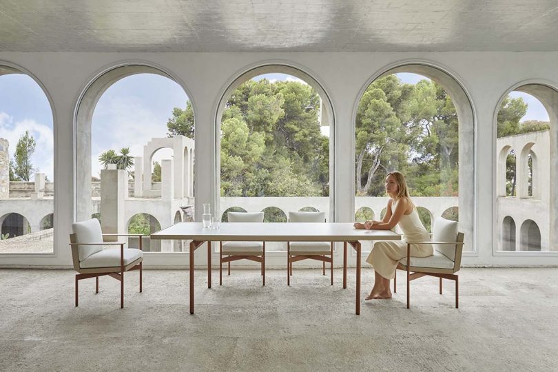 white interior space with three large arches and a dining table with seated woman