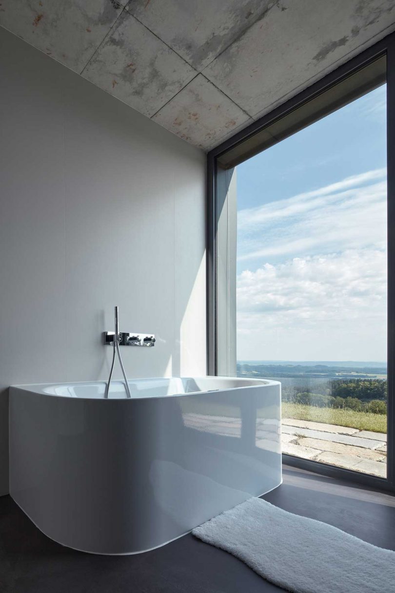 نمای زاویه دار حمام مدرن با وان مینیمالیستی با پنجره شیشه ای بزرگ