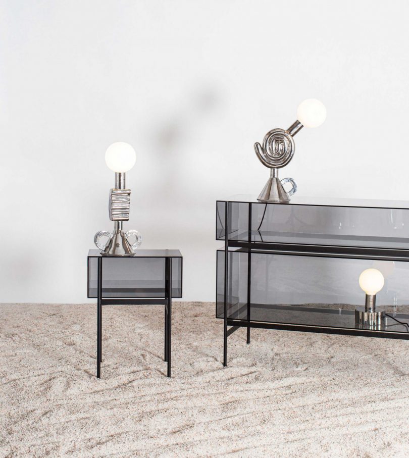 two mirrored shade-free table lamps sitting on an end table and a console table in a styled space