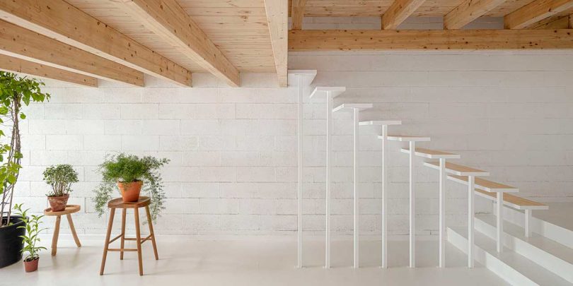 فضای داخلی خانه مینیمالیستی با سطوح سفید و جزئیات چوبی با نمای راه پله باز