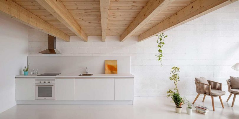 Sencillo diseño interior de una casa con encimeras blancas y detalles de madera en una cocina pequeña