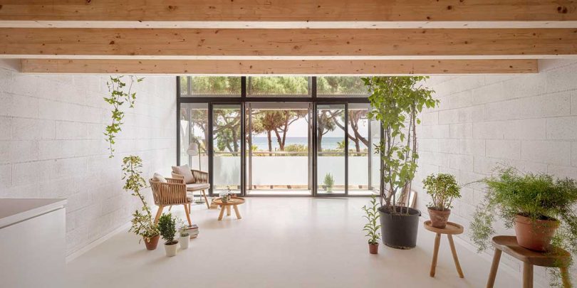 فضای داخلی خانه مینیمالیستی با سطوح سفید و جزئیات چوبی که از پنجره های جلویی به بیرون نگاه می کنند