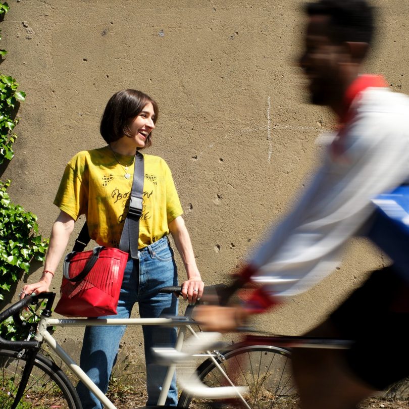 woman standing holding a white bike with red crossbody bag