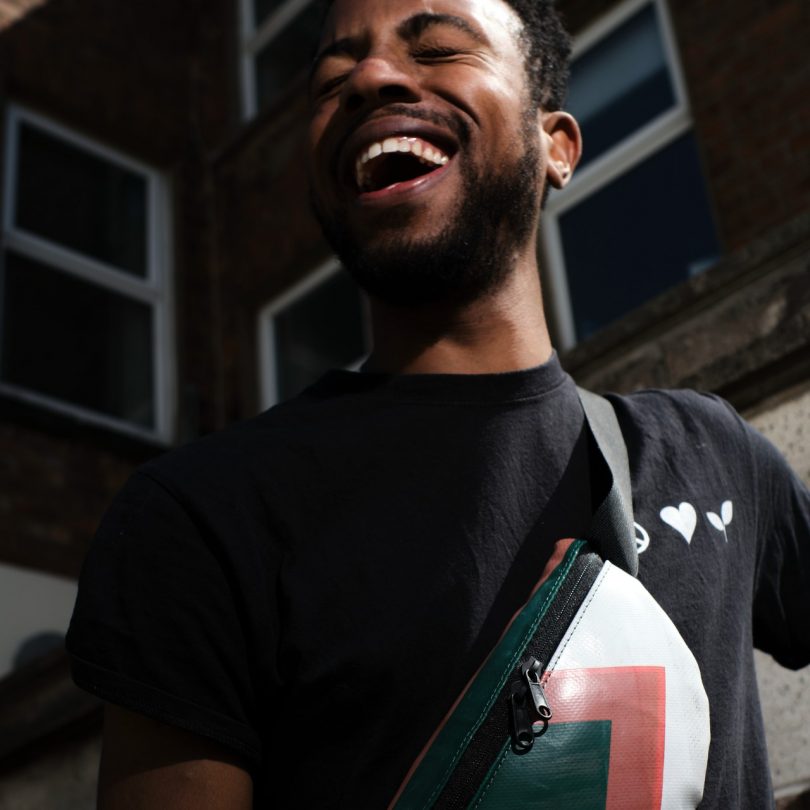 man laughing in black shirt holding a crossbody bag
