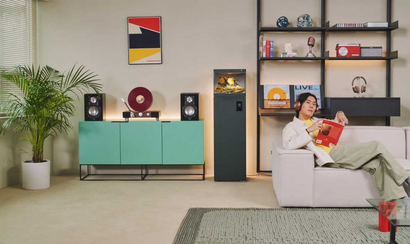 Young Asian man sitting on sofa with headphones on with LG Styler ShoeCare with yellow hi-top sneakers on display inside