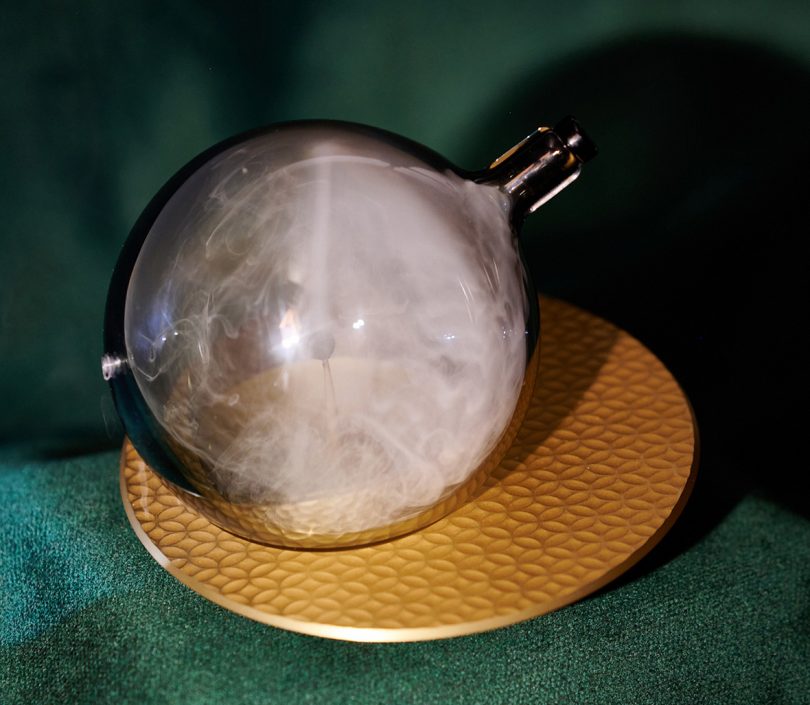 The Globe, a hand blown glass sphere displayed on table on stand with smoke inside.