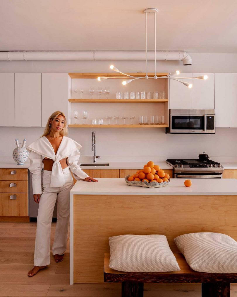styled kitchen with island, open shelves, suspended lighting, and woman posing