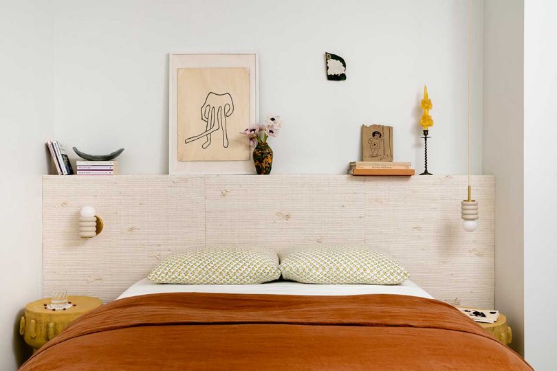 styled bedroom with above bed shelf, rust colored bedding and sconce lighting one one side, suspended lighting from the other