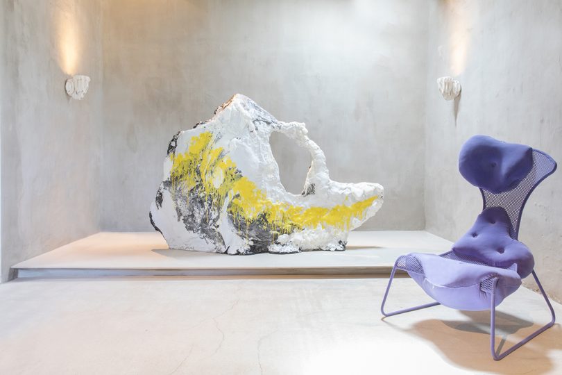 large white, yellow, and black rock-like sculpture and modern purple chair in a gallery space