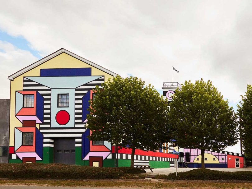 Outdoor shot of a factory building whose facade has been painted in a large, abstract patterns by Camille Walala