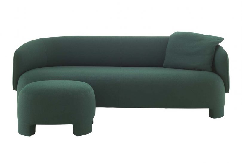 dark green upholstered sofa with pillow and ottoman on white background