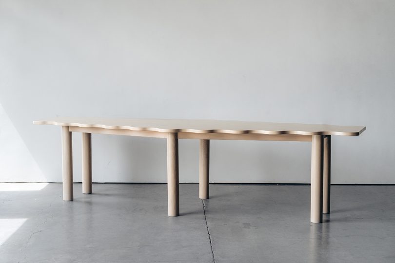 light wood diamond-shaped dining table with six legs and a wavy edge