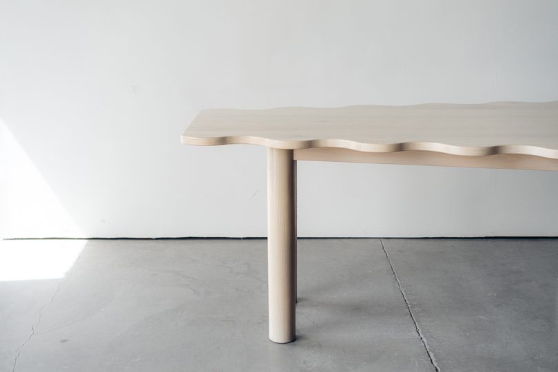 light wood diamond-shaped dining table with six legs and a wavy edge