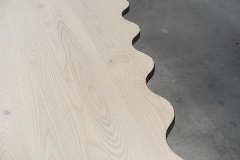 detail of light wood diamond-shaped dining table with six legs and a wavy edge