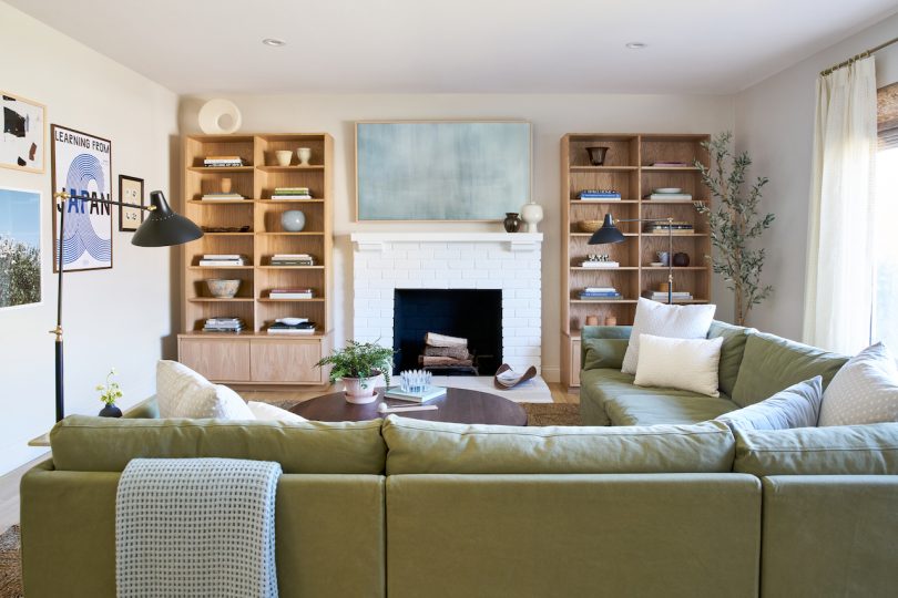 modern living room interior of Vy Yang with light green sectional and two wood bookcase flanking fireplace