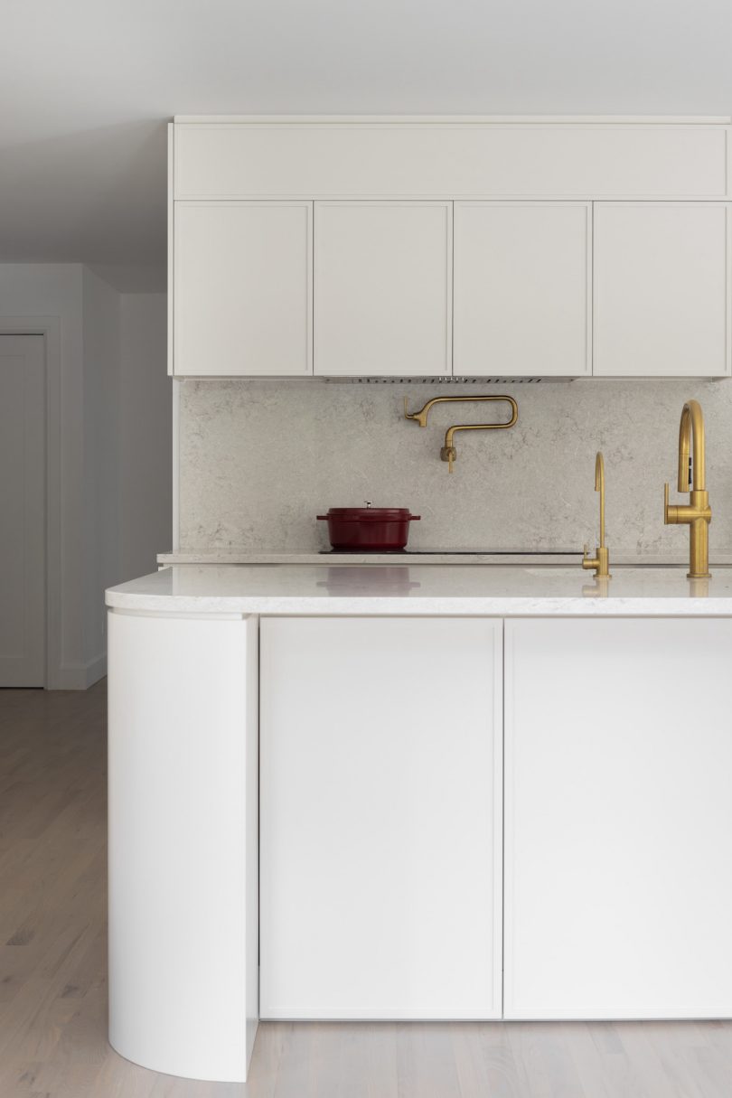 The bright kitchen features white walls, light-colored hardwood floors, quartz countertop and backsplash.