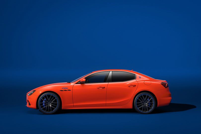 Side profile view of Maserati Ghibli F Tributo in deep orange exterior paint against blue background.