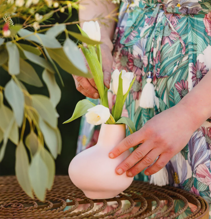 two light-skinned hands creating a flower arrangement in a small light pink vase