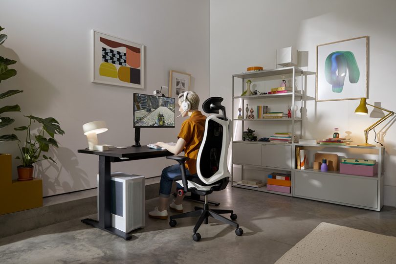 modern living space with desk setup and person sitting facing screen in a Herman Miller chair