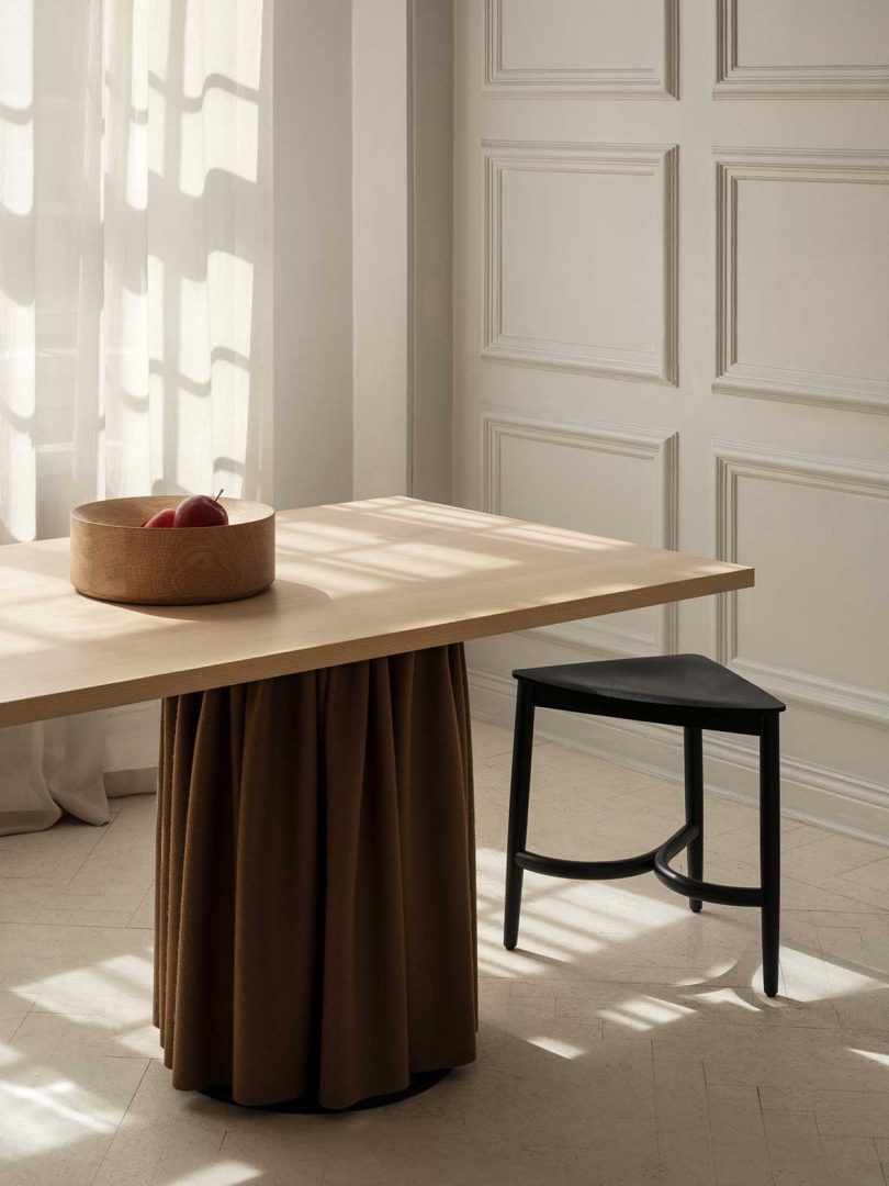 triangular short black stool tucked under a wood dining table