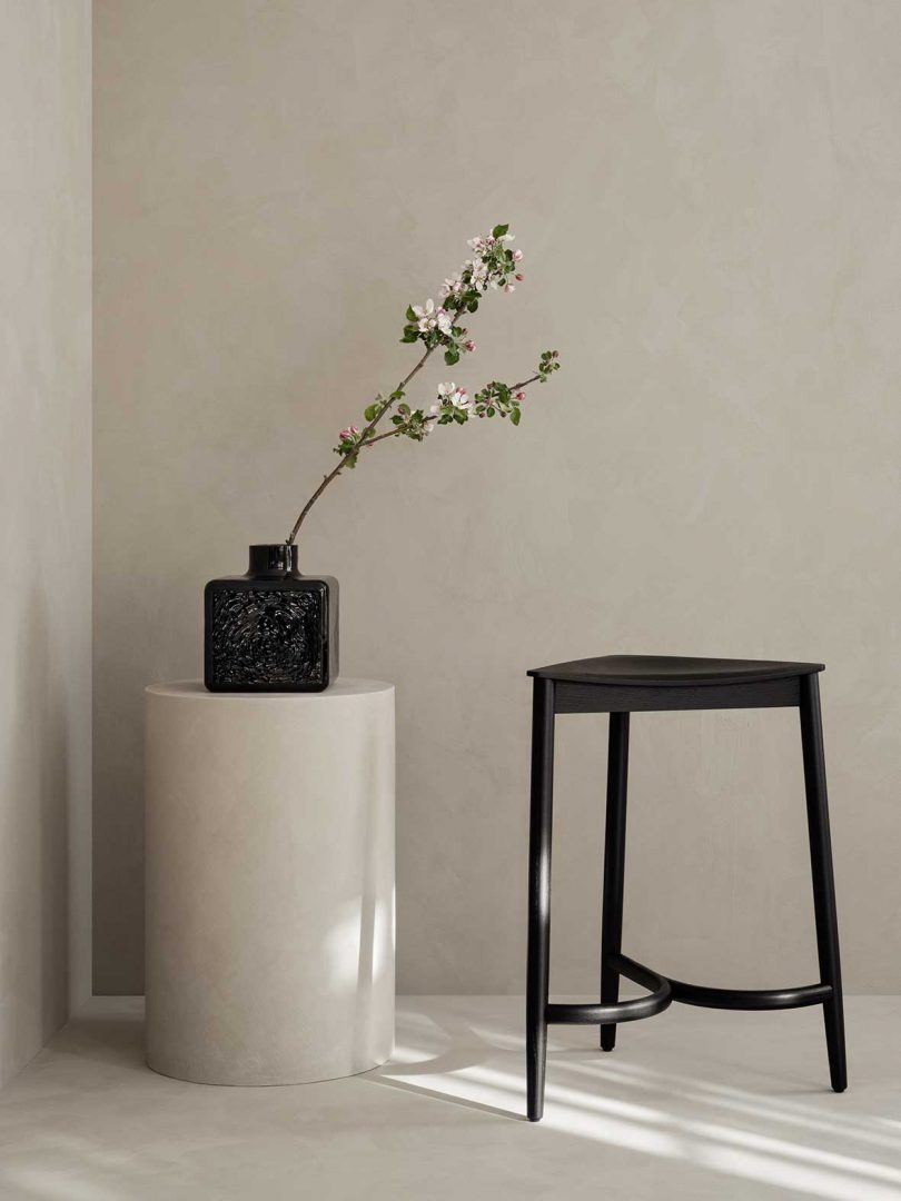 triangular black stool next to a plinth holding a vase of flowers