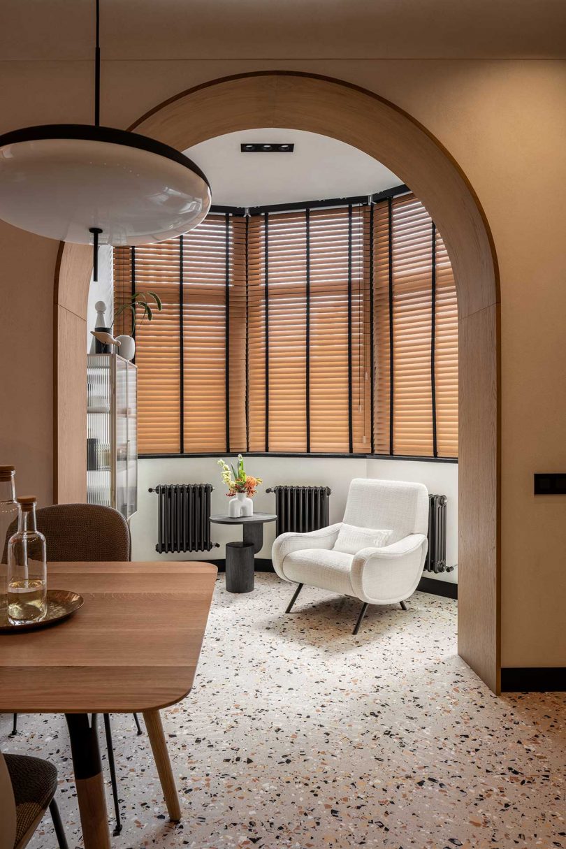 نمای داخلی آپارتمان مدرن آشپزخانه با کابینت های چوبی روشن و کف ترازو و گوشه ای با صندلی سفید