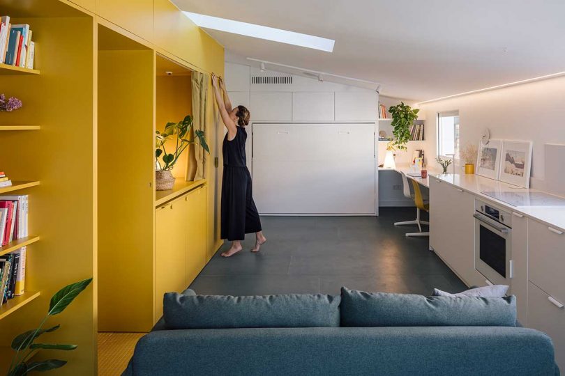 long interior shot of modern apartment with one side white kitchen and other side yellow shelving