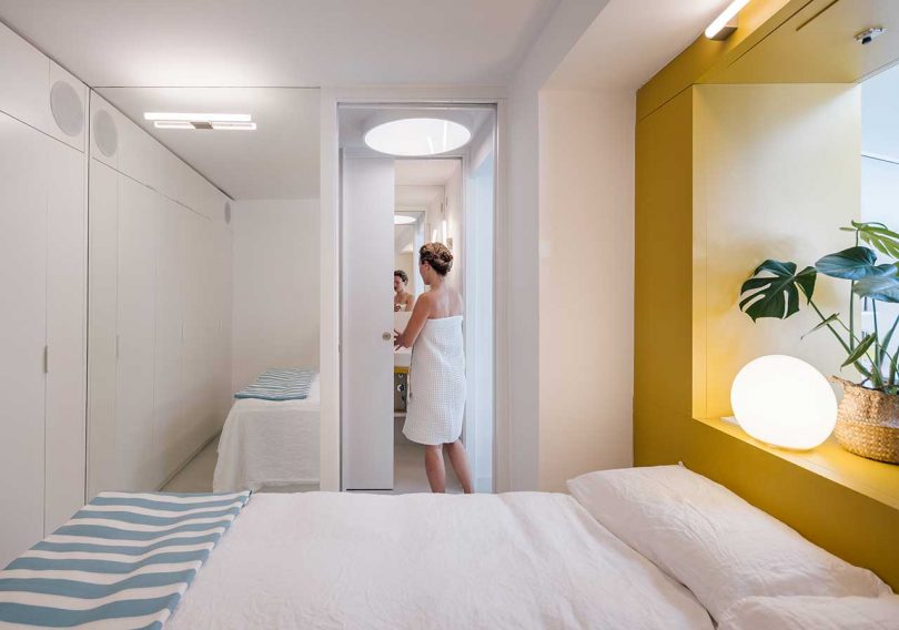woman in towel in small bathroom connected to small white bedroom