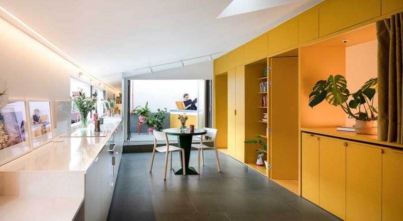 long shot of apartment interior with white kitchen on one side and yellow storage on the other