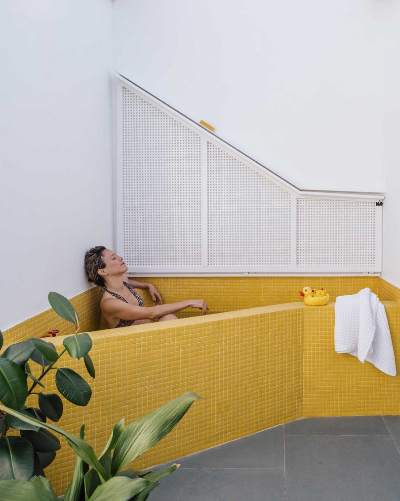 view to outside rooftop deck with woman sitting in outdoor bathtub