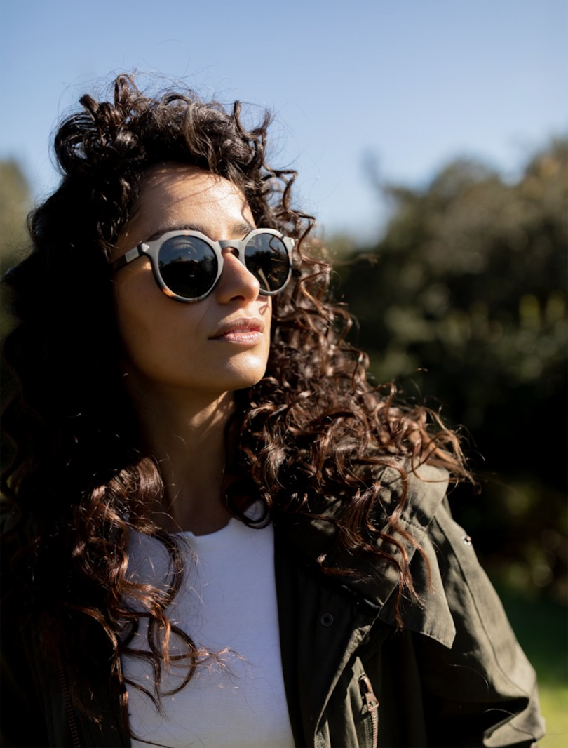 light-skinned woman with dark curly hair wearing sunglasses and looking towards the sun