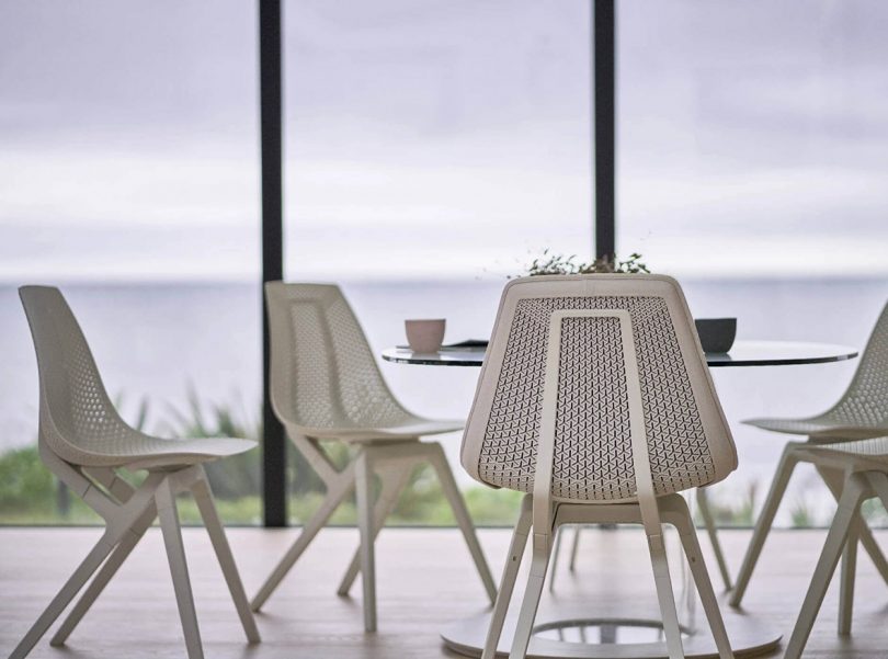 several white dining chairs gathered around a dining table with a backdrop of large windows and water beyond
