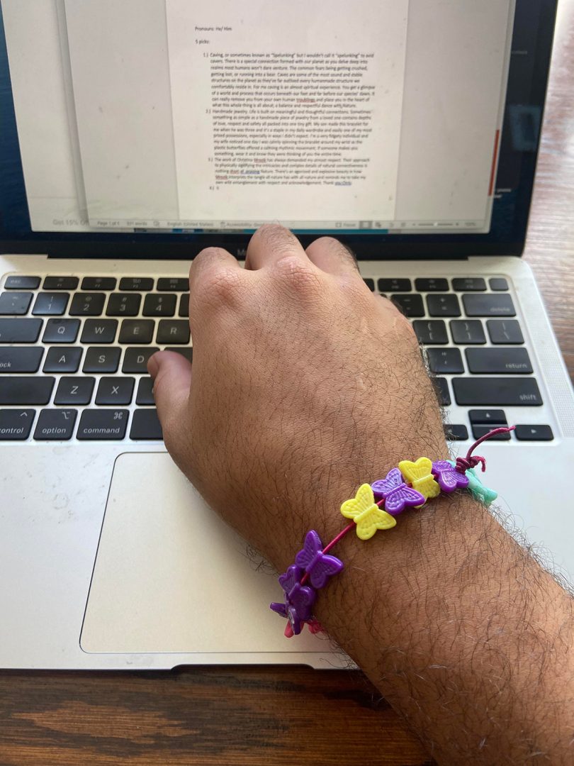 an arm wearing a butterfly bead bracelet while using a laptop