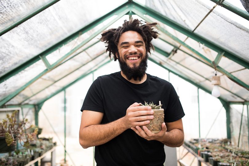 brown-skinned man with dreadlocks wearing a black t-shirt and holding a planter