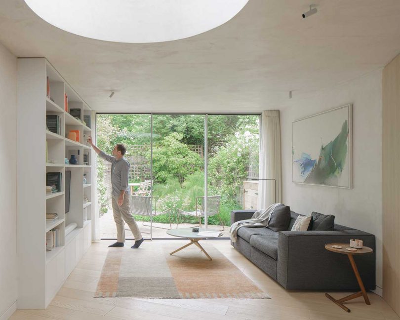 light interior of modern living room with large round skylight and man putting book on shelf