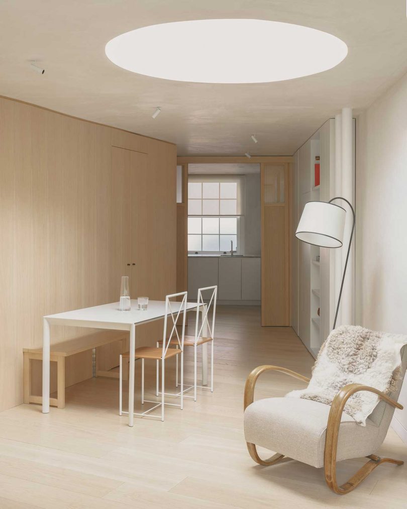 نمای داخلی اتاق نشیمن سبک با صندلی و میز ناهار خوری زیر نورگیر بزرگ سفید