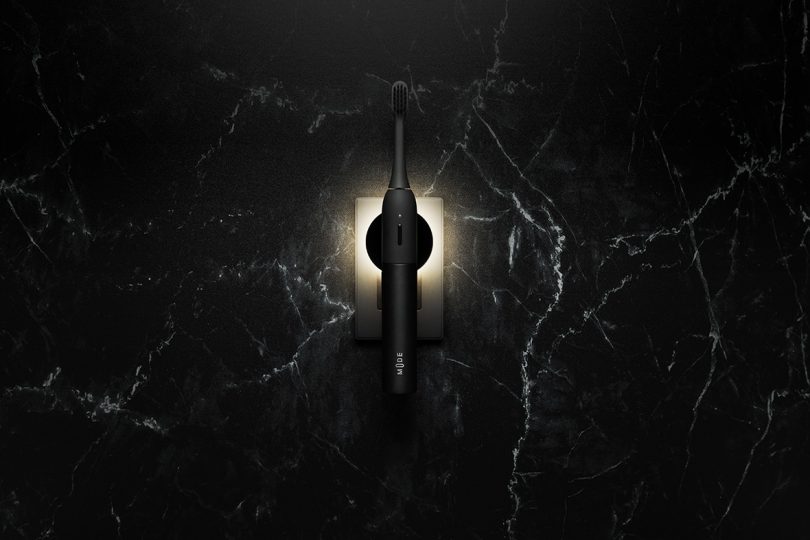 minimalist black electric toothbrush plugged into wall outlet with light shining behind