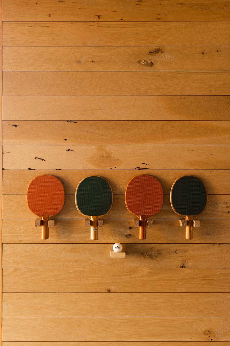 wood paneled wall holding shelf with four ping pong paddles and ball