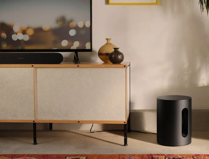 Black Sonos Sub Mini shown to the right of a media console with flat panel television and Ray sound bar. 