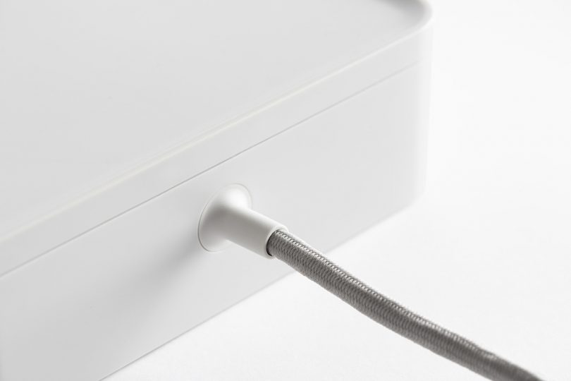 Detail of textile braided power cord of Ampli charging station in white against white background.