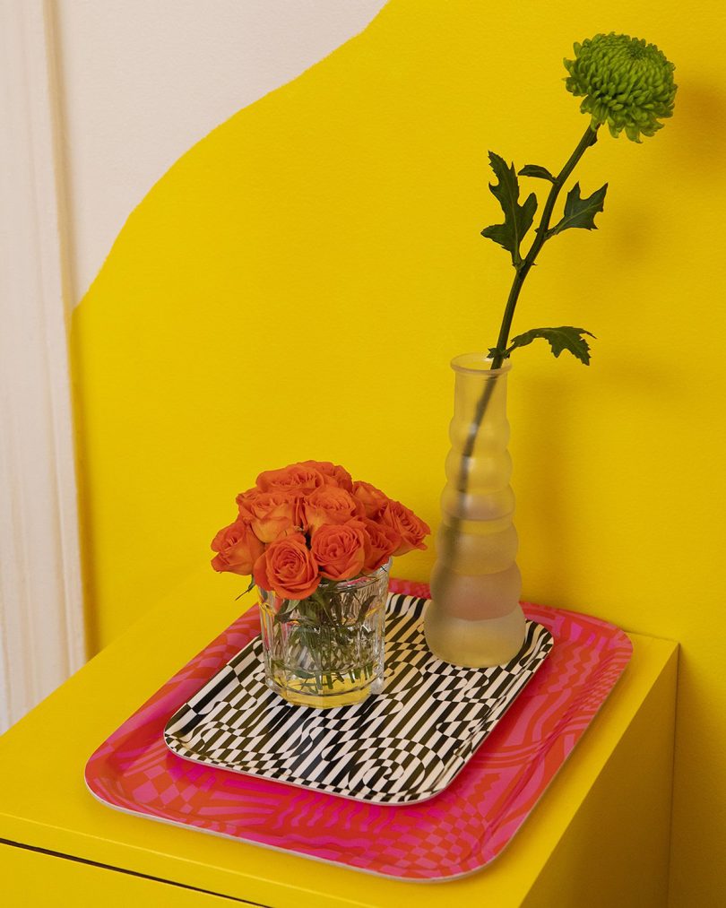 black and white zebra print tray, red tray, and two glass vessels with flowers in front of a yellow wall