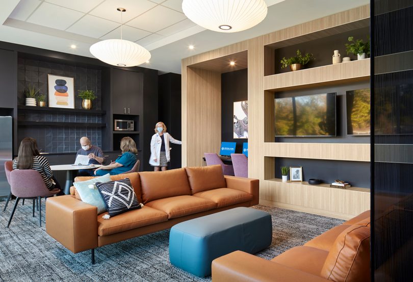 modern medical waiting area with rust colored sofas, a blue coffee table, and suspended lighting