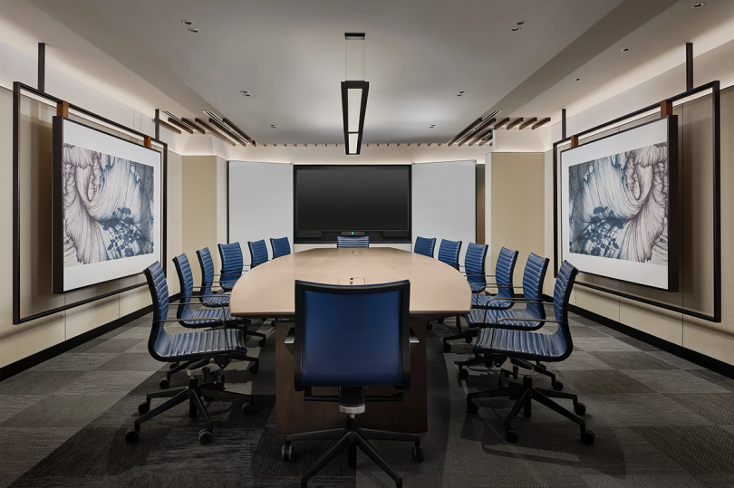 meeting room with long light wood table, 14 rolling chairs, and a large screen