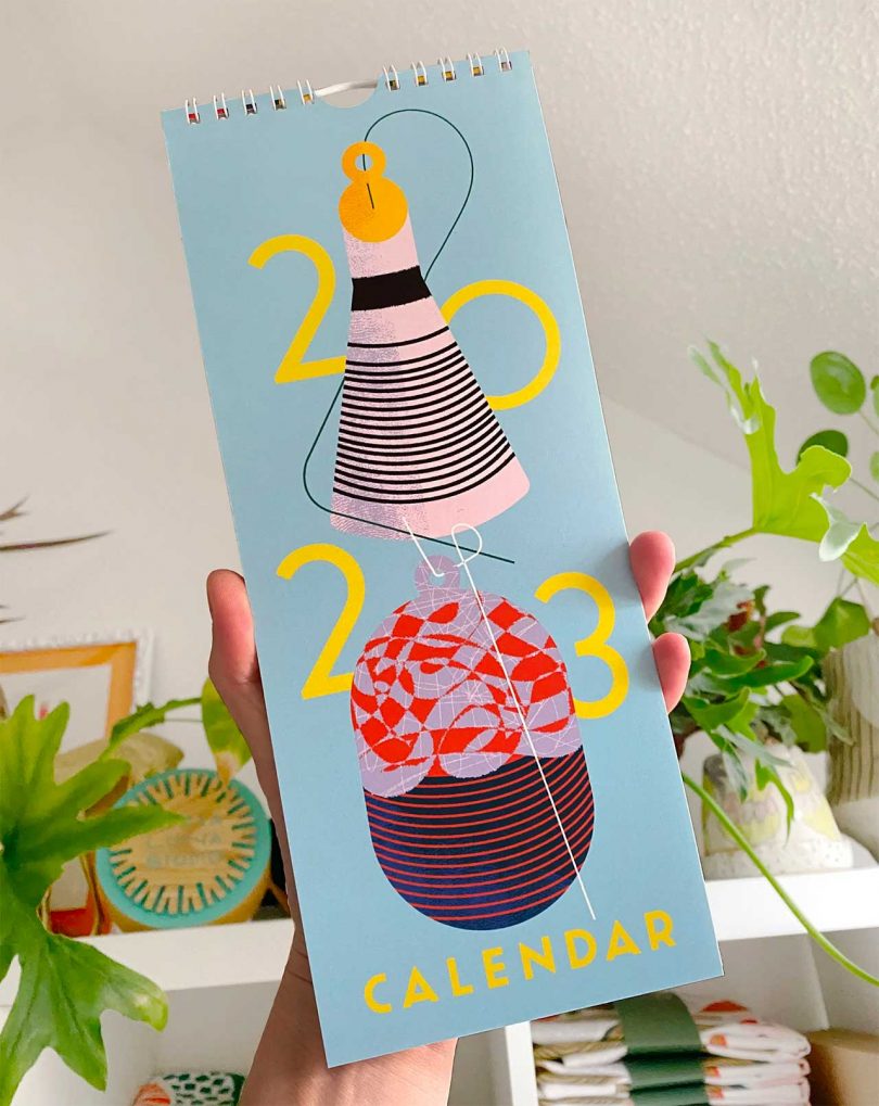 hand reaching out holding an elongated 2023 calendar with colorful images on front