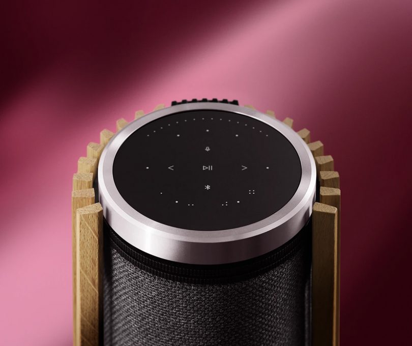 Detail of Beolab 28 floor speaker from angled top view showing touch panel controls and wood louvre cover against pink background.