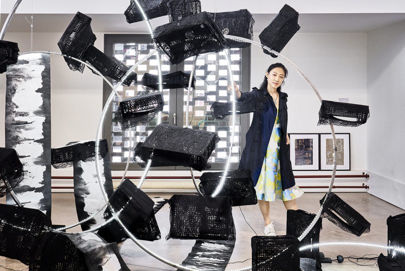 futuristic black and metal circular object with light-skinned woman wearing a long black coat