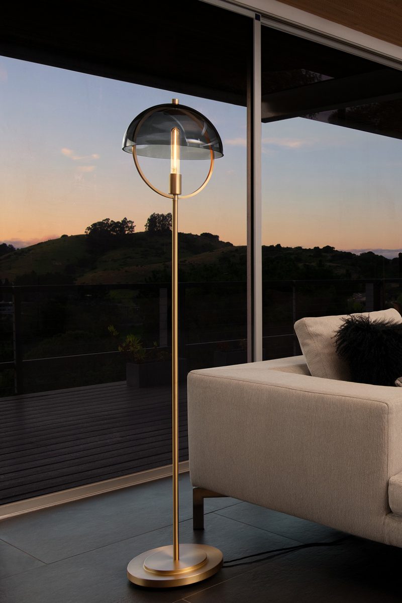 Floor lamp edition from the Copernica Collection shown in darkened living room set besides sofa, with the last remaining minutes of a sunset in the background.